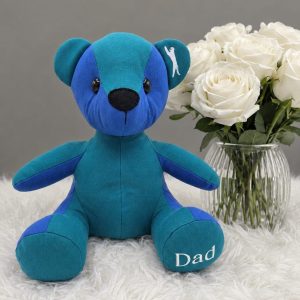 Blue and teal standard memory bear with Dad embroidered on its paw, beside white roses