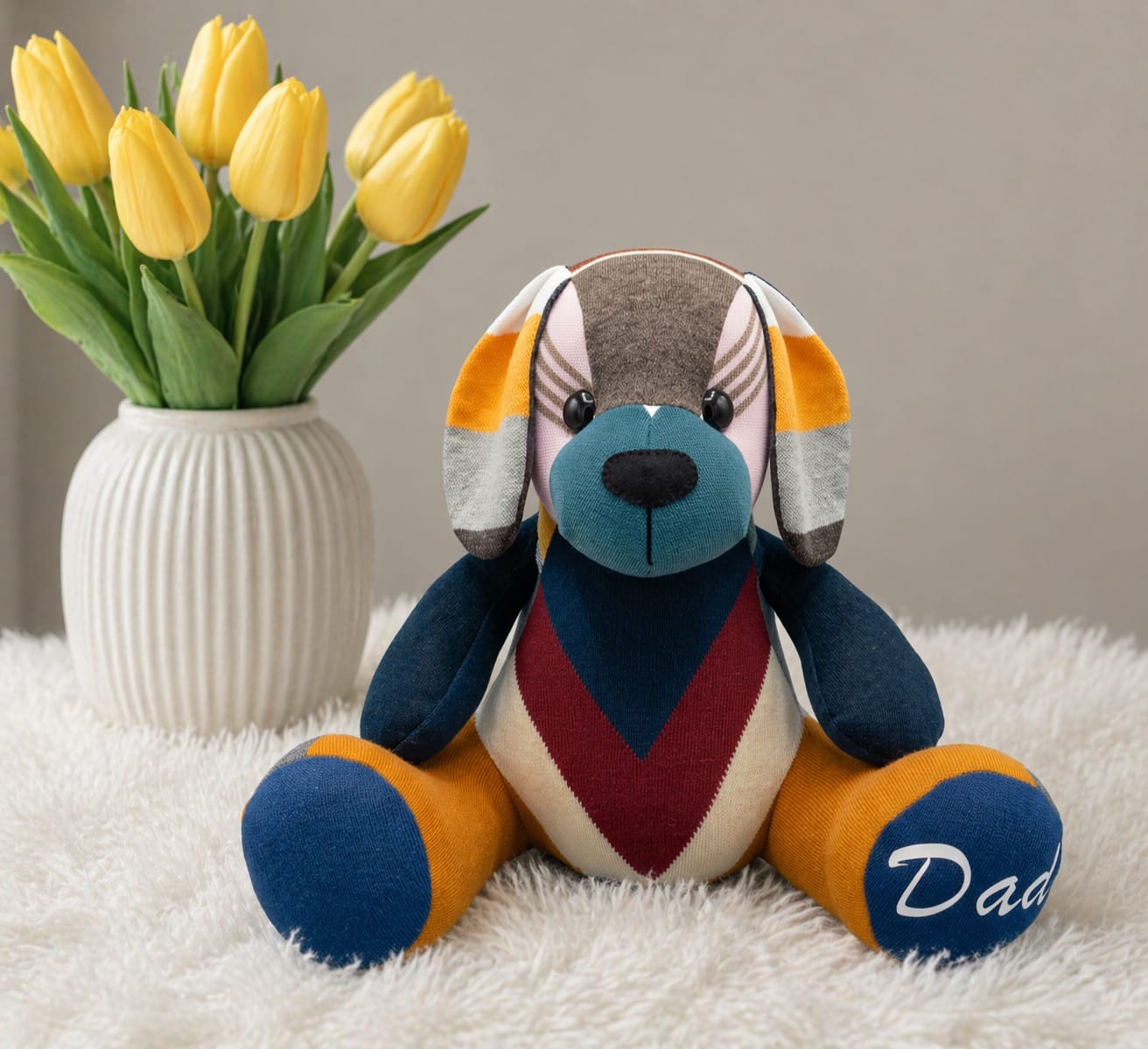 Patchwork memory puppy with floppy ears beside a vase of yellow tulips