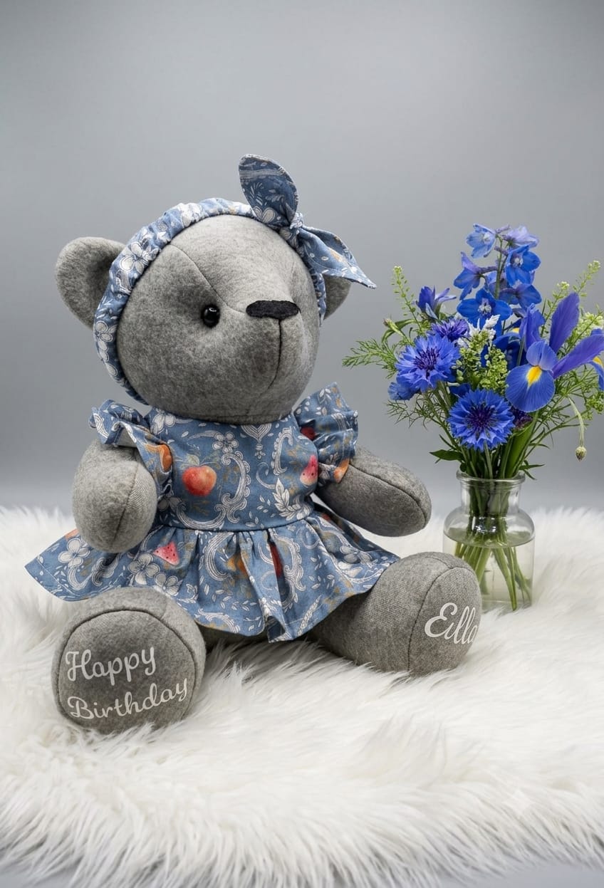 Small grey memory bear wearing a blue floral dress and matching headband