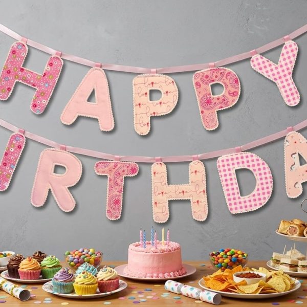 Pink patchwork Happy Birthday fabric banner above a party table with cake and treats
